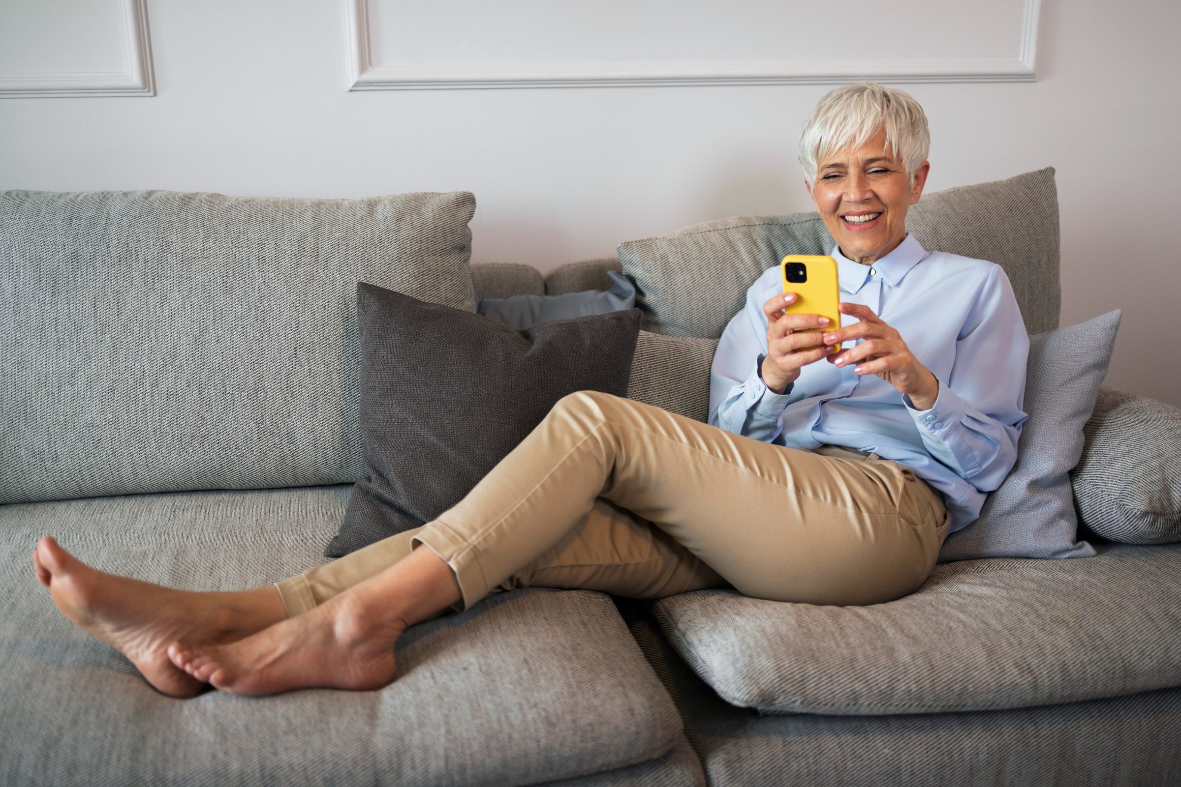 A smiling woman relaxing on a sofa, looking at her phone