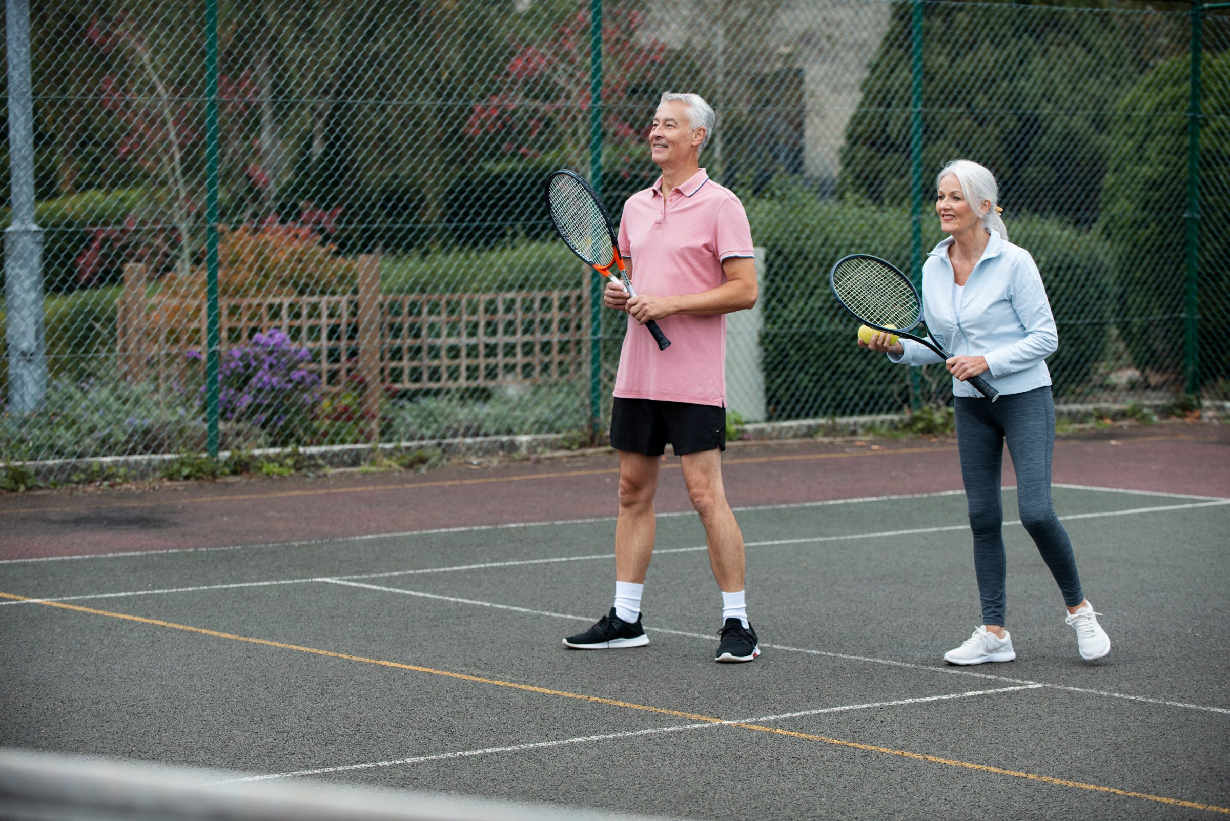 An older couple smiling on a tennis court, rackets in hand